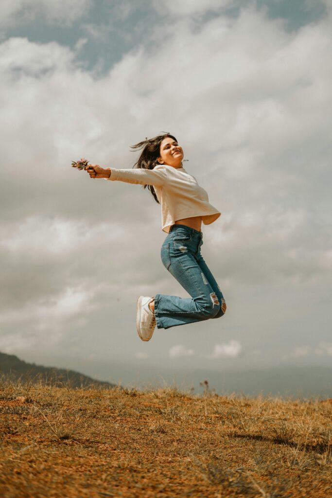 Frau springt voller Energie auf einer Wiese – steht für mehr Vitalität und Wohlbefinden durch eine ausgewogene pflanzliche Ernährung.