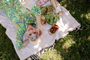 A stylish senior woman in a colorful dress enjoying a picnic with fresh fruits and a scenic view.