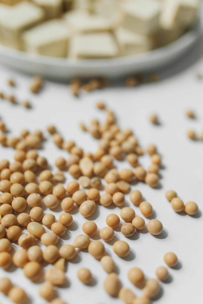 A close-up view of soybeans scattered on a white surface with a dish in the background.