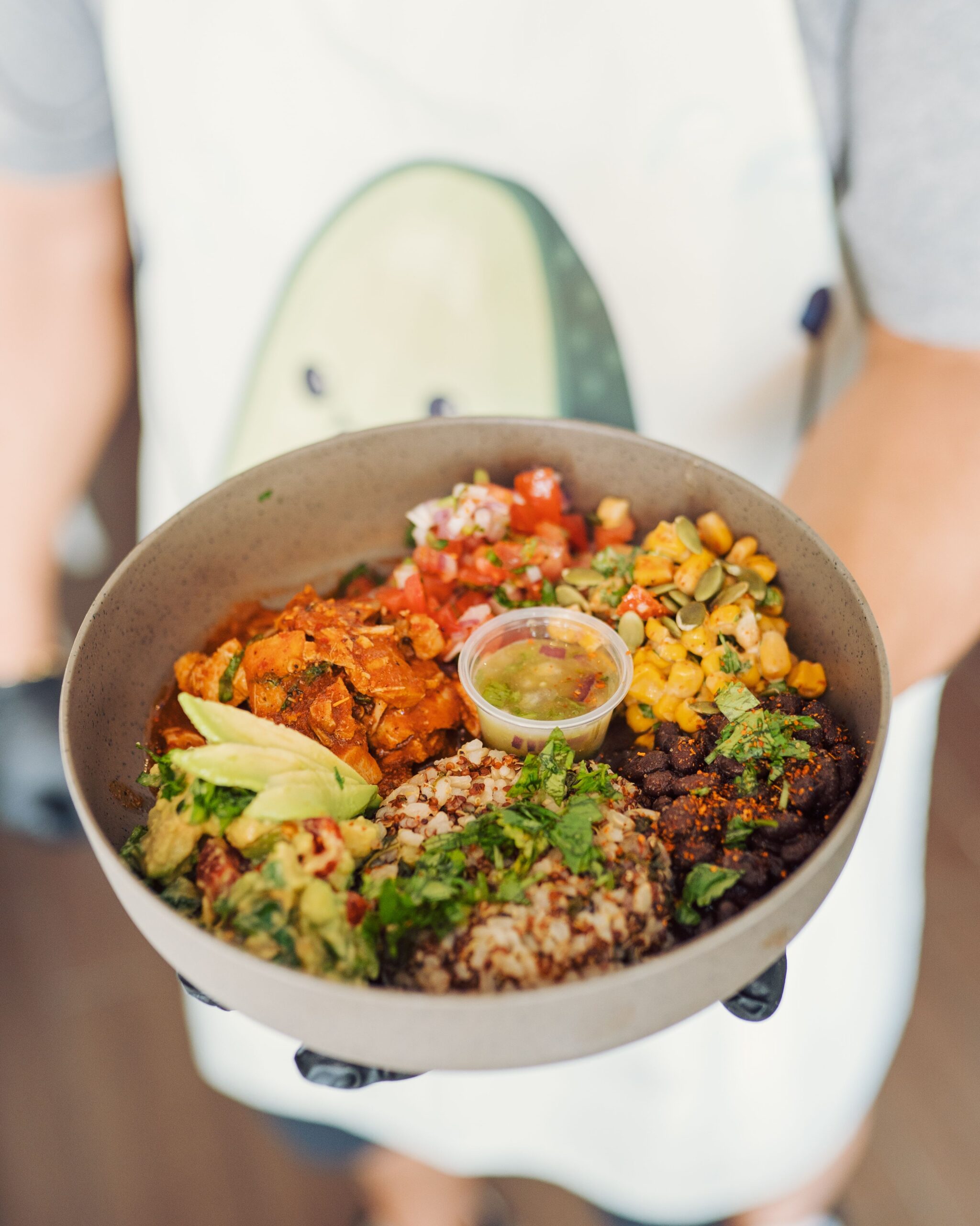 Colorful Mexican-inspired meal with avocado, quinoa, salsa, and more, held by a person with a decorated apron.
